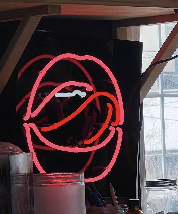 Neon sign of a mouth with red lips on a black background, on the wall of Maggie's art Studio